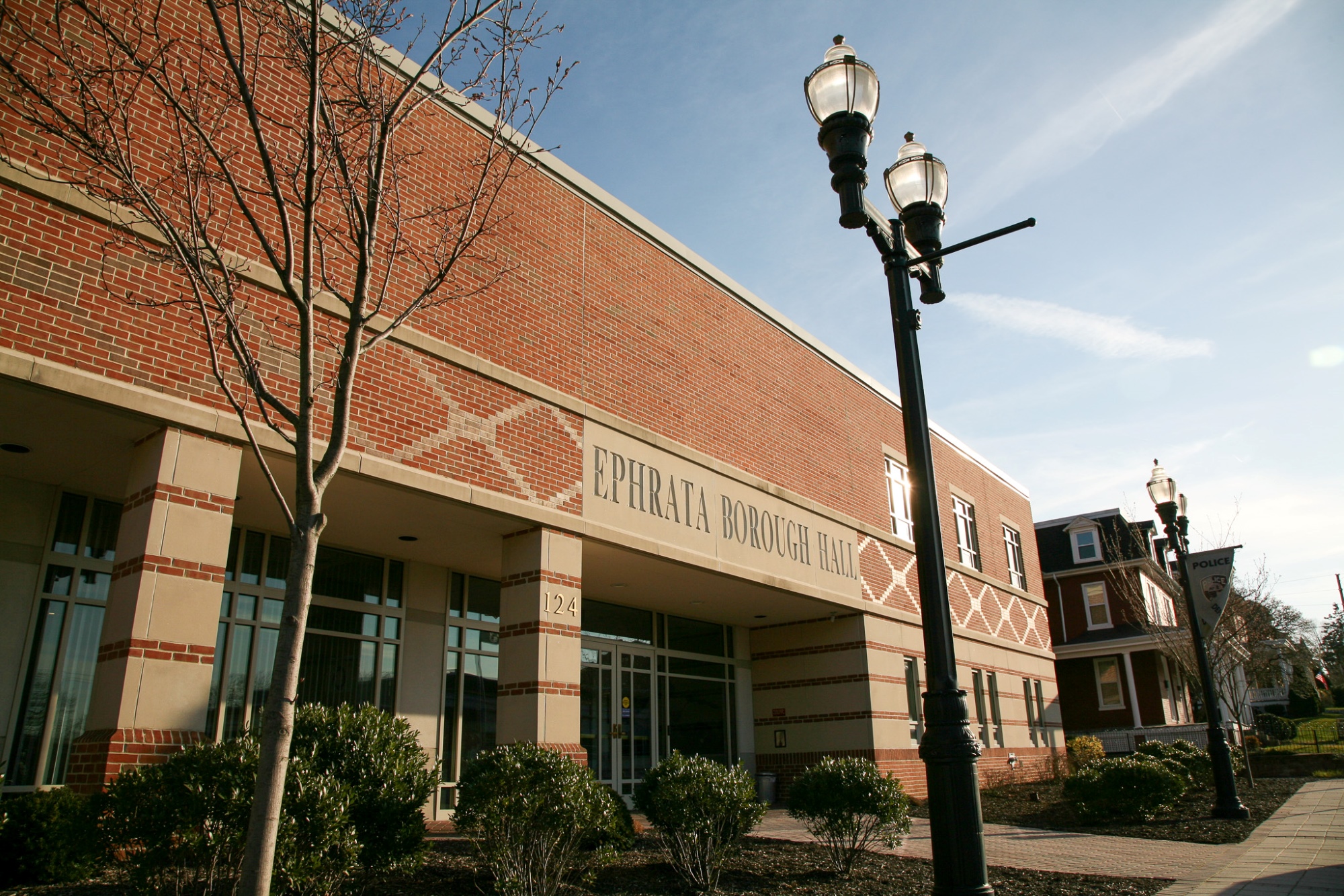 Ephrata Borough Hall, a brick municipal building with patterned masonry, glass entrance doors and black streetlamps along a landscaped sidewalk under a clear sky.