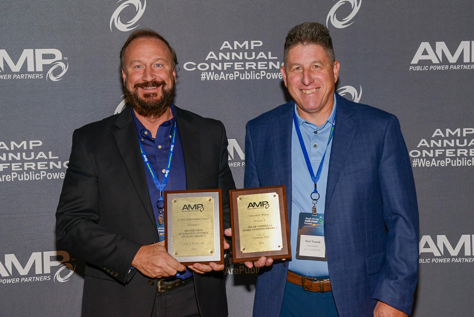 Two smiling recipients of AMP's Innovation Award holding their congratulatory plaques.