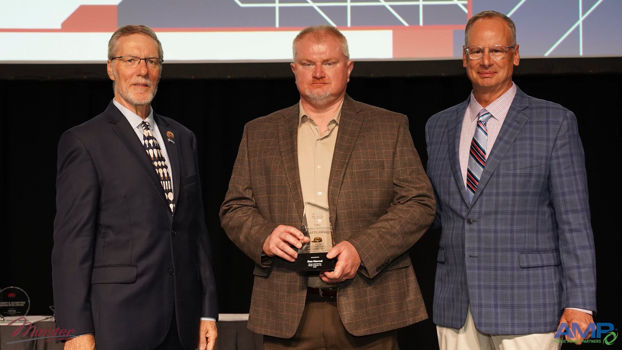 Three individuals stand on a stage during an awards ceremony, with the center individual holding a glass trophy. The award recognizes Don Harrod with the APPA Seven Hats Award. The two individuals on either side wear business suits, and a large presentation screen with graphic elements and partial text is visible in the background.