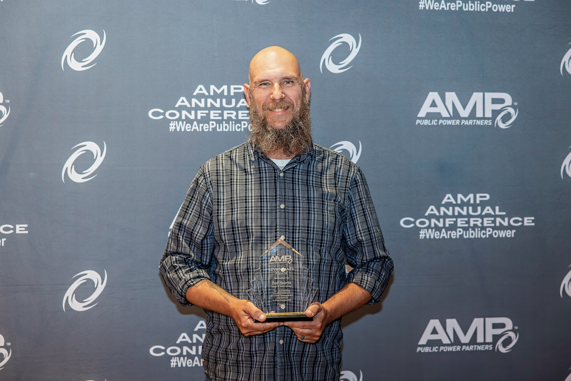 Ben Sparks hold his AMP Seven Hats Award trophy in front of a photo backdrop